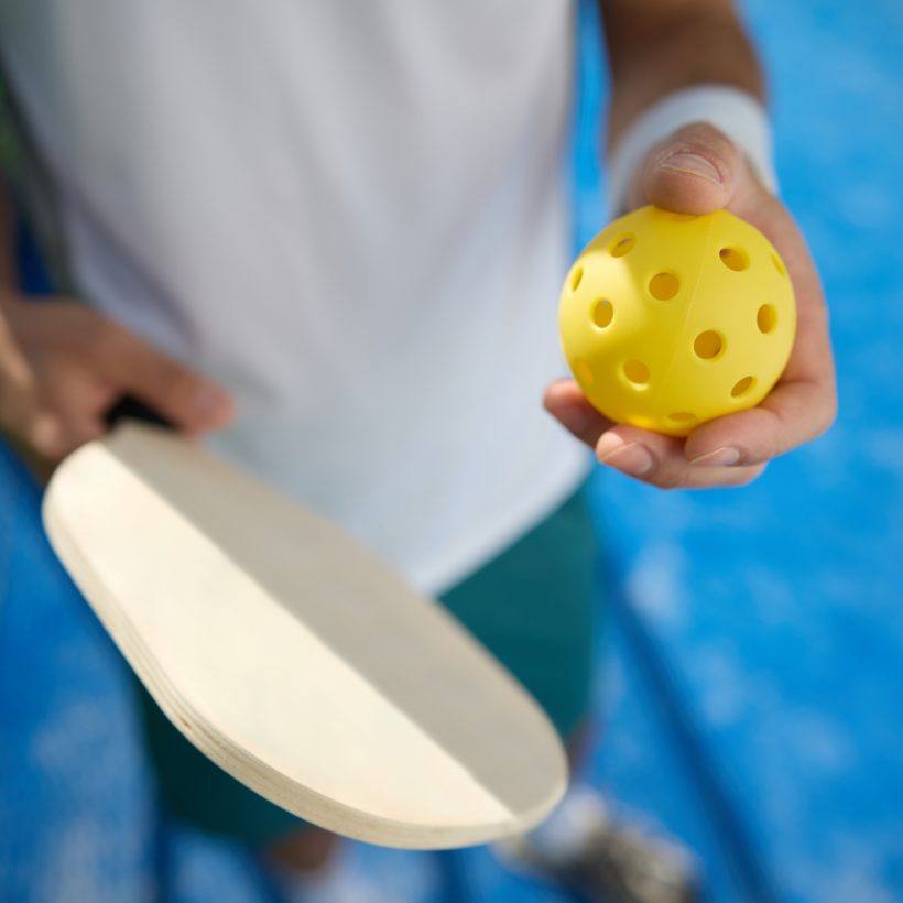 Close up of player with ball and pickleball paddle on an outdoor court.